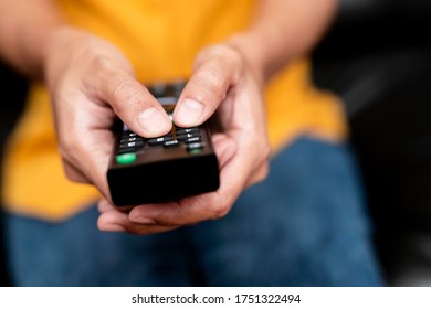 The hand is pressing the remote control to select the channel.Spend leisure time at home watching a movie.