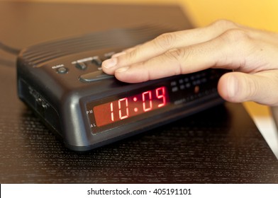 Hand Pressing The Snooze Button On A Digital Alarm Clock
