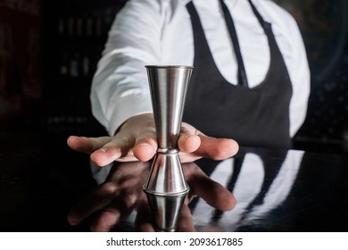 The hand of a professional bartender holds a jigger tool or measuring cup to control the ingredients added to the cocktail.
