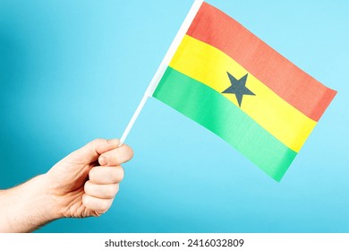 A hand is prominently waving the red, yellow, and green flag of Ghana. - Powered by Shutterstock