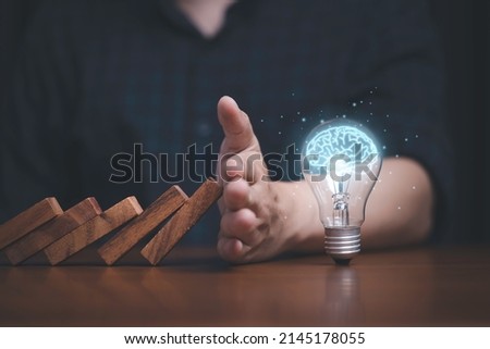 Hand protecting lightbulb with glowing virtual brain from falling wooden block , It is symbol of protect copyright and patent concept.