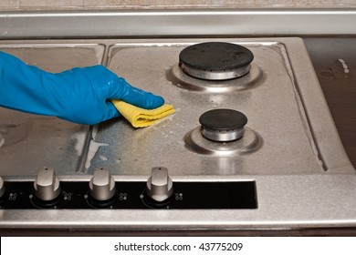 Hand In Protective Blue Glove Is Polishing A Gas Stove With Yellow Duster