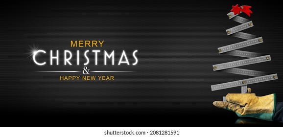 Hand with protective work glove holding a small metallic ruler in the shape of a Christmas tree with a red comet star, on a black background with text Merry Christmas and Happy New Year.