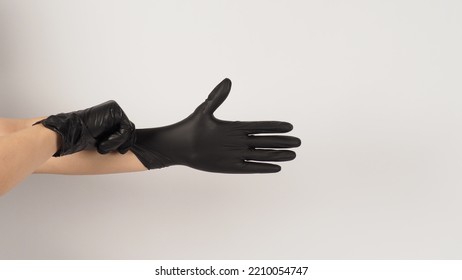 The Hand Is Pulling Black Latex Gloves  On White Background.