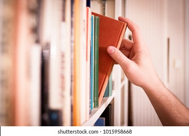Hand pulling a classic book from a library bookshelf. - Shutterstock ID 1015958668