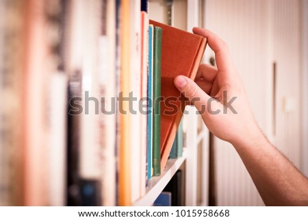 Hand pulling a classic book from a library bookshelf.