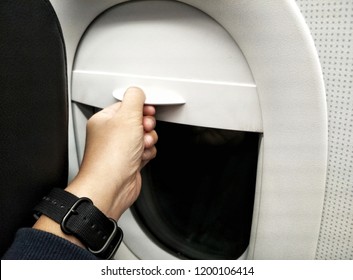 Hand pulling down aircraft window curtain while travelling on flight is blurry.