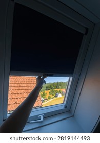 Hand pulling down blackout blind on skylight window for room darkening and sun protection