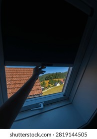 Hand pulling down blackout blind on skylight window for room darkening and sun protection