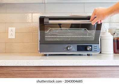 Hand pulling down a digital countertop oven door