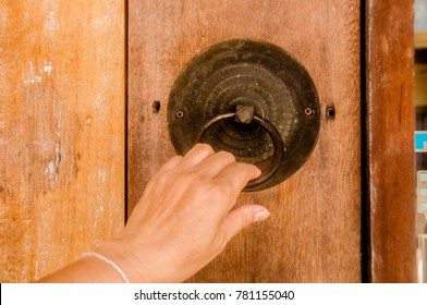 ?A hand pulling metal ring knocker on vintage wooden door.