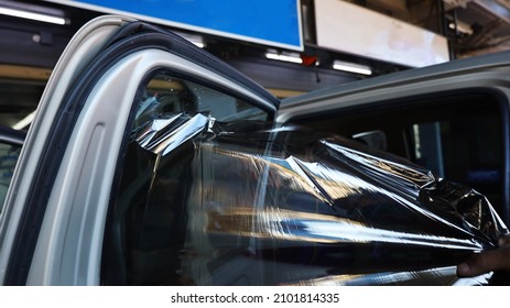 Hand Pulling The Old Film Out Of The Car Windshield. Peeling Off The Window Tinting Film To Install A New Film In The Auto Shop. Close Up,Selective Focus