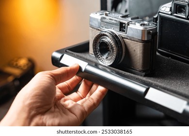 A hand pulling out a camera storage drawer containing a vintage camera and a modern SLR camera.