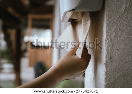 Hand pulling paper towel from a wall-mounted dispenser, highlighting hygiene, cleanliness, and hand drying routine in a modern indoor setting.