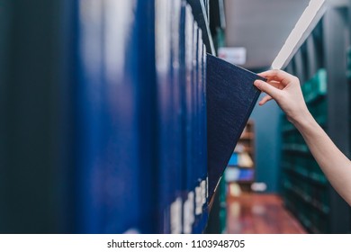 Hand pulling a Thesis book off the shelf in Library. Green colors books.