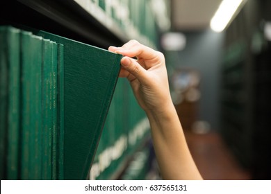 Hand pulling a Thesis book off the shelf in Library. Green colors books. - Shutterstock ID 637565131