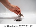 Hand pulls hair out of bathroom drain. Female palm extracts shock of hair from siphon in bathroom. Water drain hole clogged with hair clump. Close up. Cleaning shower polluted sewerage system.