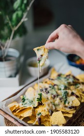 Hand pulls out a cheesy nacho chip from platter. Sharing homemade Mexican comfort food with friends and family. Authentic people cooking a vegetarian healthy snack at home. Casual lifestyle.