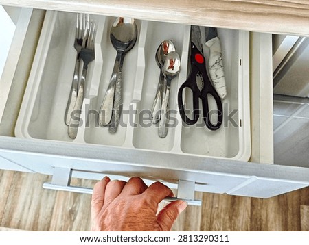 A hand pulls out a kitchen drawer filled with forks, spoons, knives, and scissors. This scene shows a typical moment of daily life at home.