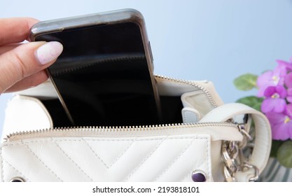 A Hand Pulls Out A Phone From A Small White Bag.