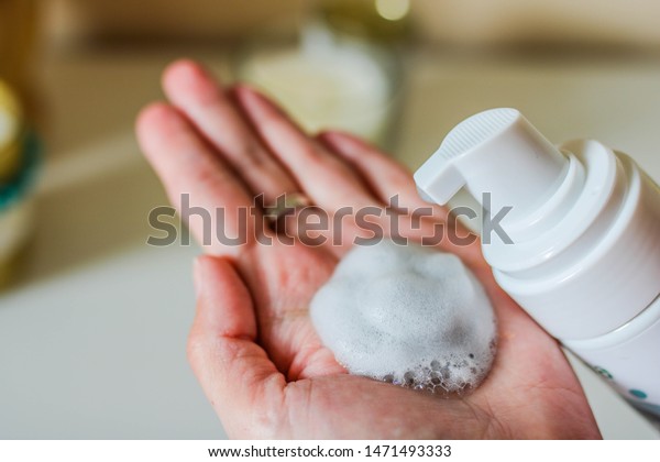 Hand pumping\
cleansing foam, Face cleanser, Cosmetics foam pump container. White\
blurred background.