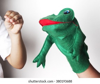 Hand Puppet Of A Funny Green Frog Playing With A Child Hand Isolated On White Background.