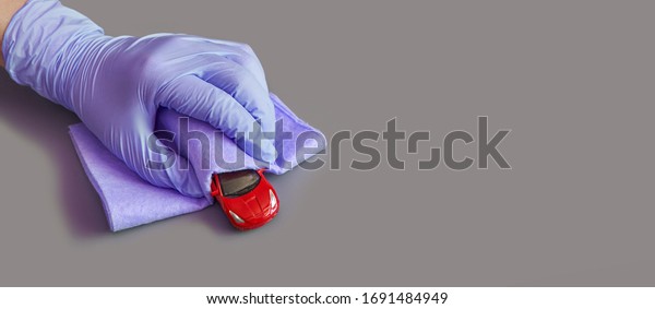 Hand in purple glove\
holding red toy car. Safety anti virus and dust concept. Mother do\
antibacterial cleaning at child room. Anti virus hygiene procedure.\
Grey background