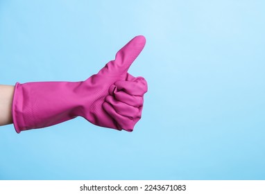 Hand in purple rubber cleaning glove shows thumbs up on blue background. House cleaning and housekeeping concept