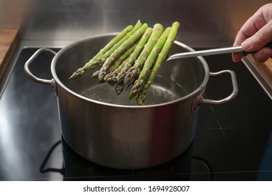 Hand Puts Green Asparagus On A Skimmer In A Pot With Boiling Water For A Holiday Dinner, Healthy Cooking Concept, Copy Space, Selected Focus, Narrow Depth Of Field