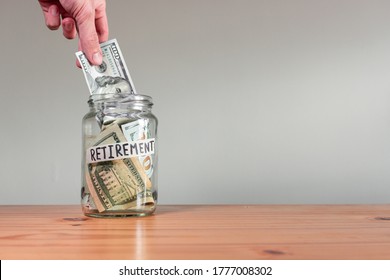 Hand puts Money US Dollar bills in a glass jar labeled "retirement". 401k saving concetp