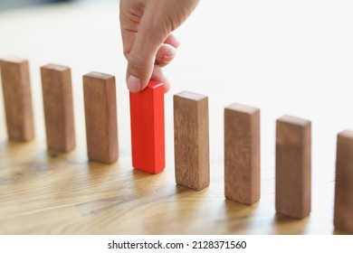 The Hand Puts A Red Wooden Block In A Row With Brown Ones, Close-up. The Concept Of Choosing A Startup, Setting Priorities