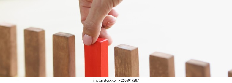 The Hand Puts A Red Wooden Block In A Row With Brown Ones, Close-up. The Concept Of Choosing A Startup, Setting Priorities