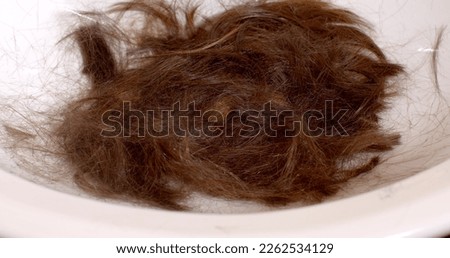 A hand puts scissors on cut hair on a white background. The end of the haircut, the accumulation of hair for processing into a wig. Preparation for the manufacture of artificial hair.