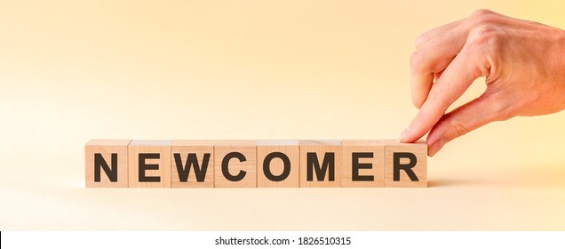 The hand puts a wooden cube with the letter R from the word NEWCOMER. The word is written on wooden cubes standing on the yellow surface of the table. - Shutterstock ID 1826510315
