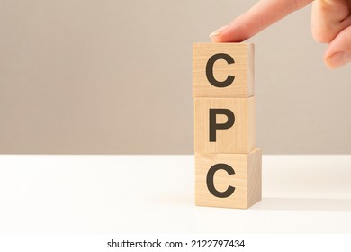 the hand puts a wooden cube with the letter CPC - short for Cost Per Click. business concept. space for text in left. front view