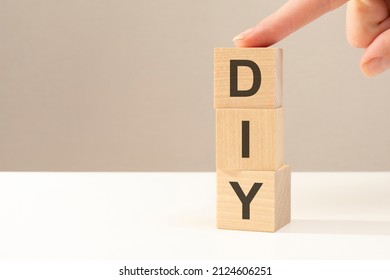 The Hand Puts A Wooden Cube With The Letter DIY - Short For Do It Yourself. Business Concept. Space For Text In Left. Front View