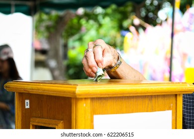 Hand putting banknote into a wooden box as donation at a Thai Buddhist temple.