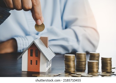 Hand putting coin in house model of coin for saving money for buying house. Savings plans for home, loan, investment, mortgage, finance and banking about house concept.