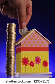 Hand Putting A Coin Into A House Shaped Money Box