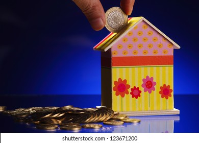 Hand Putting A Coin Into A House Shaped Money Box