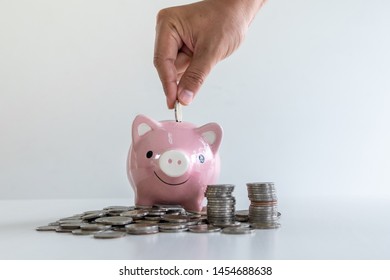 hand putting a coin into pink piggy bank with coins pile, step up growing business to success and saving for retirement concept. 