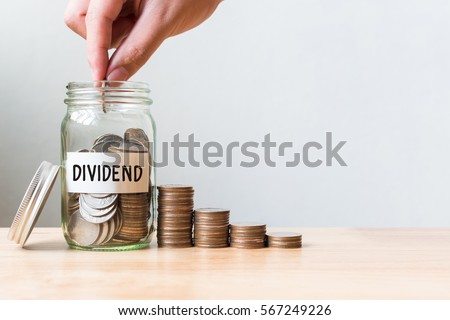 Hand putting coin in jar word dividend with money stack, Concept business finance and investment
