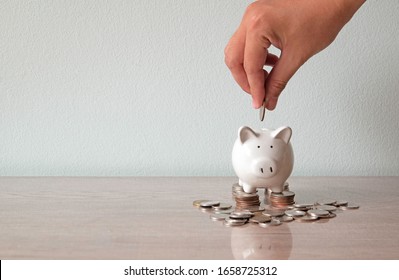 Hand, die dem Sparschwein und dem Sparschwein die Münze zuschiebt, steht auf dem Münzhaufen. Sparen des Geldkonzepts. 