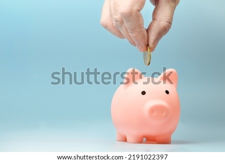 Hand putting coin to pink piggy bank on a blue background. Copy space