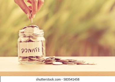 Hand putting Coins in glass jar with DONATE word written text label for giving and donation concept
