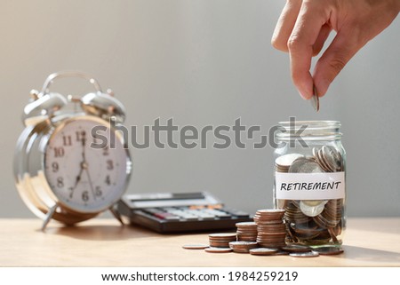 Hand putting Coins in glass jar with calculator and alarm clock for time to money saving for retirement concept ,  retirement planning.