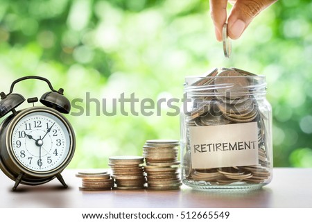 Hand putting Coins in glass jar for with retro alarm clock  for time to money saving for retirement concept