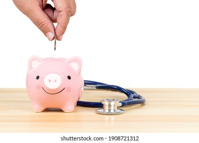 Hand Putting Depositing Money Into Pink Piggy Bank With Stethoscope On Wooden Desk On White Background, Concept Financial Health Check And Retirement Fund And Insurance