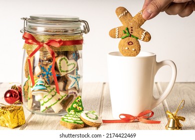 Hand Putting Gingerbread Man Cookie Into A Mug With A Christmas Cookies Jar On The Side With White Background