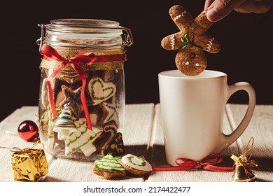 Hand Putting Gingerbread Man Cookie Into A Mug With A Christmas Cookies Jar On The Side With Black Background